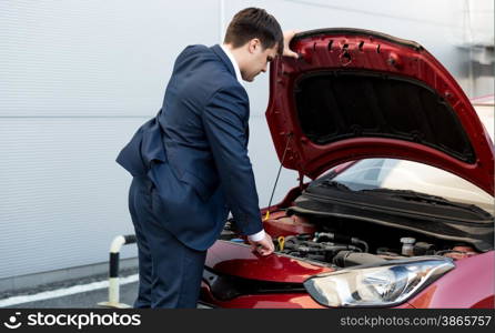 Young businessman in suit opening bonnet of open car