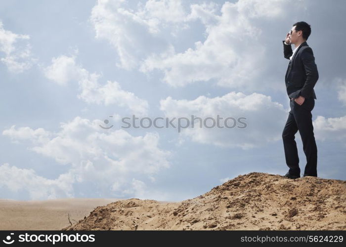 Young businessman in sunglasses standing in the desert and talking on the phone