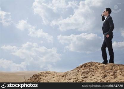 Young businessman in sunglasses standing in the desert and talking on the phone
