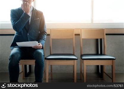 young businessman in waiting room for job interview being anxious, on a row of chairs