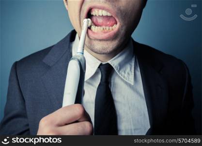 Young businessman is brushing his teeth with an electric toothbrush