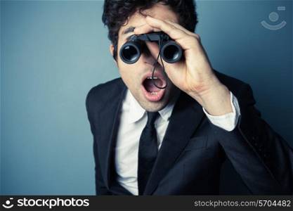 Young businessman is looking through binoculars and is surprised at what he sees