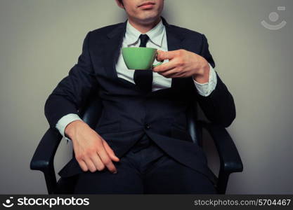 Young businessman is sitting in an office chair and drinking coffee