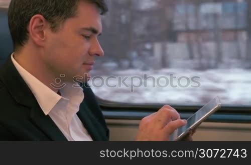 Young businessman is sitting in coach and writing letters in tablet PC.