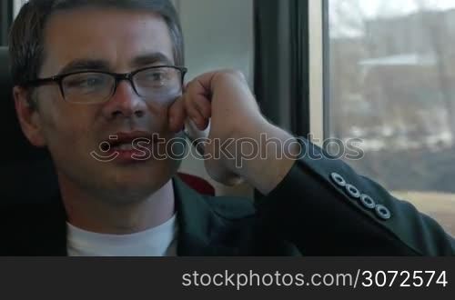 Young businessman is sitting in train and talking on the phone. After the end of conversation he&acute;s looking out the window.