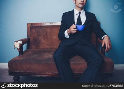 Young businessman is sitting on a sofa drinking coffee