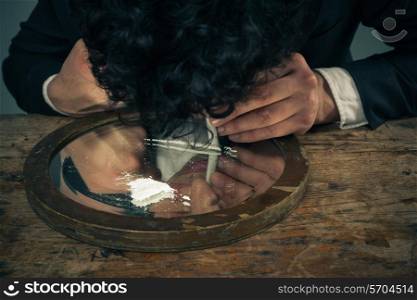 Young businessman is snorting cocaine with a rolled up banknote
