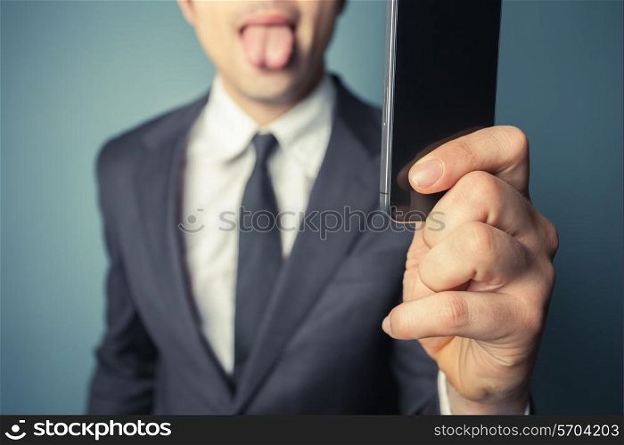 Young businessman is taking a selfie with his smart phone and sticking his tongue out