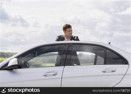Young businessman leaning on broken down car at countryside