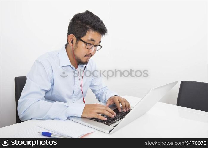 Young businessman listening music while using laptop in office