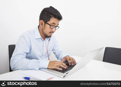 Young businessman listening music while using laptop in office