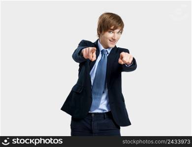 Young businessman looking and pointing to the camera, over a gray background