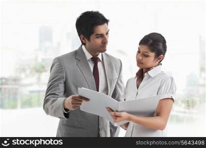 Young businessman looking at female colleague with document in hand