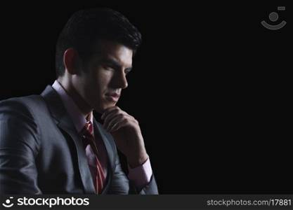 Young businessman looking away against black background