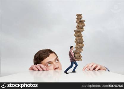 Young businessman looking from under table at man carrying pile of books