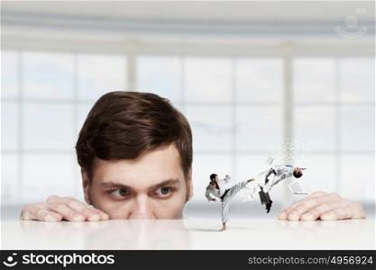 Young businessman looking from under table on fighting people. Businessman peeping from under table