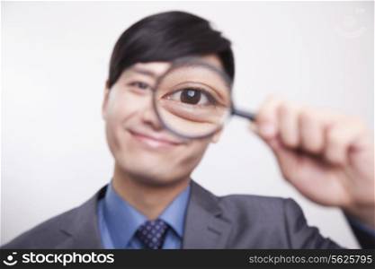Young businessman looking through magnifying glass, studio shot