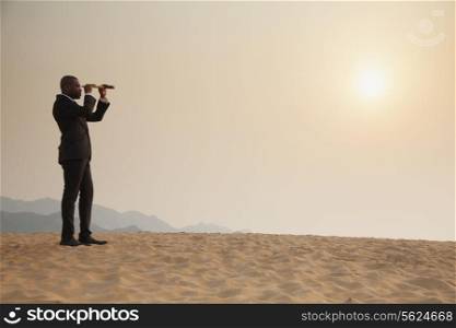 Young businessman looking through telescope in the middle of the desert