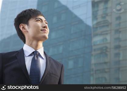 Young Businessman Looking Up, Glass Building, Portrait