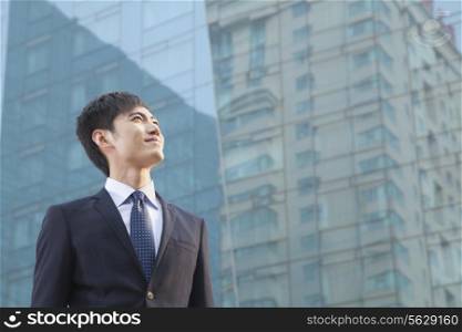 Young Businessman Looking Up, Glass Building, Portrait