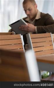 Young businessman on a coffee break. Using tablet computer. Focus on chairs