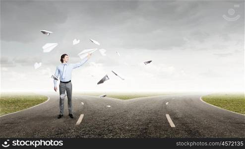 Young businessman on asphalt road with paper plane in hand