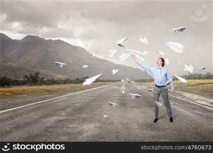 Young businessman on asphalt road with paper plane in hand