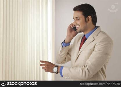 Young businessman on call while looking through window blinds