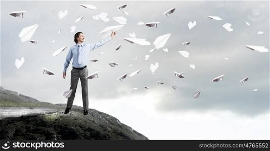Young businessman on rock top with paper plane in hand