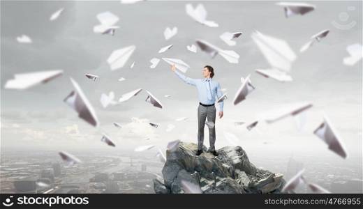 Young businessman on rock top with paper plane in hand