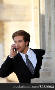 Young businessman on the phone by a stone building