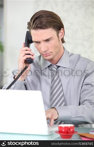 Young businessman on the phone while using his laptop