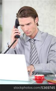 Young businessman on the phone while using his laptop