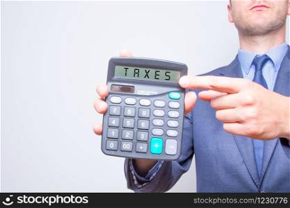 Young businessman pointing on calculator. Taxes business concept Calculator with TAXES on display