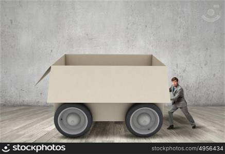 Young businessman pushing carton box on wheels. Box on wheels