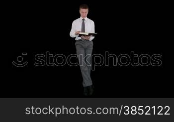 Young businessman reading a book and sitting, against black