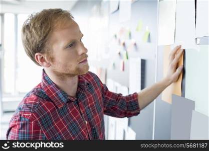 Young businessman reading documents on wall at creative office