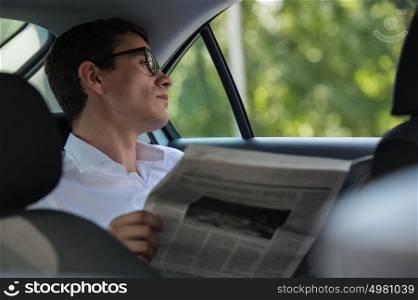 Young businessman reading newspaper on back seat of his car