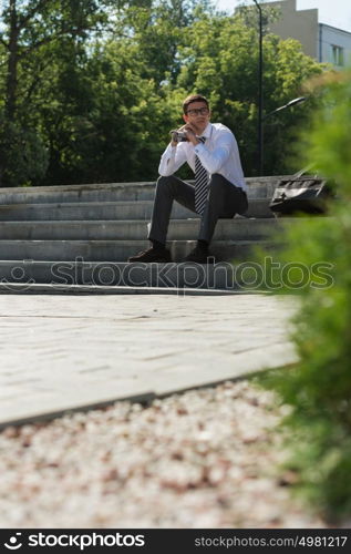 Young businessman resting in sunlight on stairs outdoors and thinking