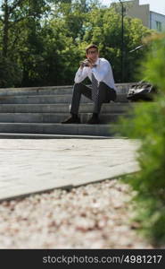 Young businessman resting in sunlight on stairs outdoors and thinking