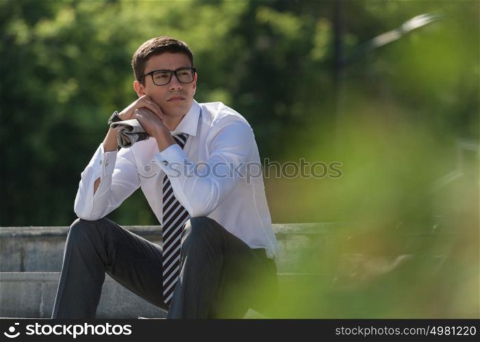 Young businessman resting in sunlight on stairs outdoors and thinking