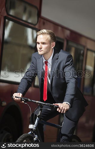 Young businessman riding bicycle by bus