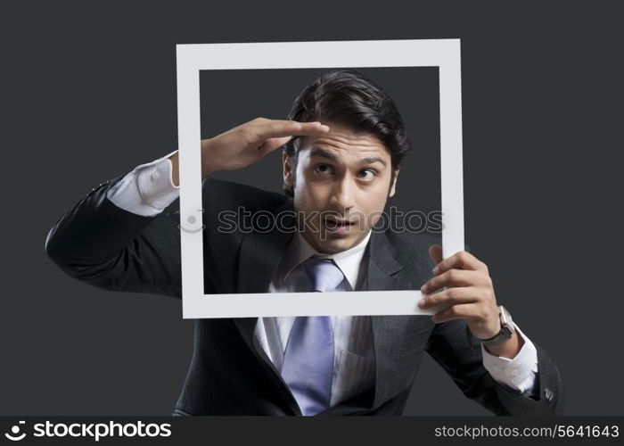 Young businessman shielding eyes while holding frame over black background