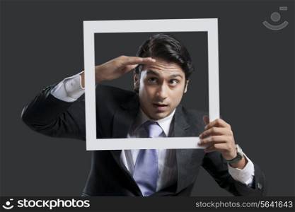 Young businessman shielding eyes while holding frame over black background