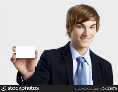 Young businessman showing and pointing to a business card, over a gray background