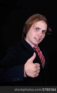 Young businessman showing thumb up in front of the black background