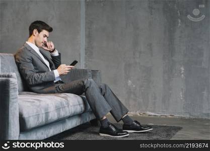young businessman sitting grey sofa using cellphone