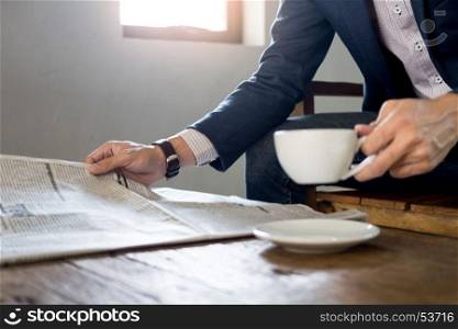 Young businessman sitting in a cafe drinking coffee and reading newspaper.