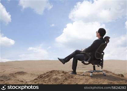 Young businessman sitting in an office chair in the middle of the desert
