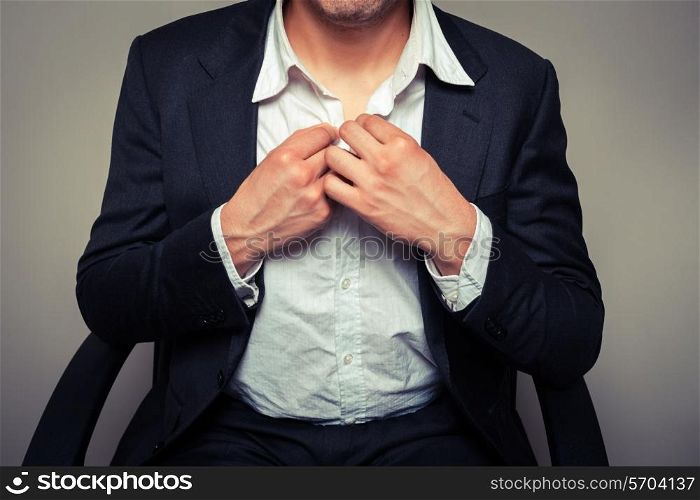 Young businessman sitting in office chair is buttoning his shirt